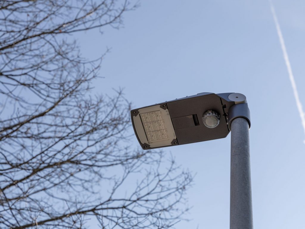 Straßenlampe mit Bewegungssensor von unten vor blauem Himmel fotografiert.